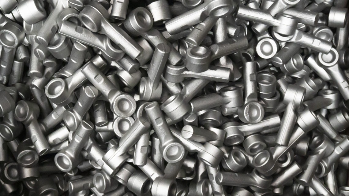 The image shows a dense collection of metallic parts, possibly automotive components, with cylindrical shapes and hollow centers, in monochromatic tones.