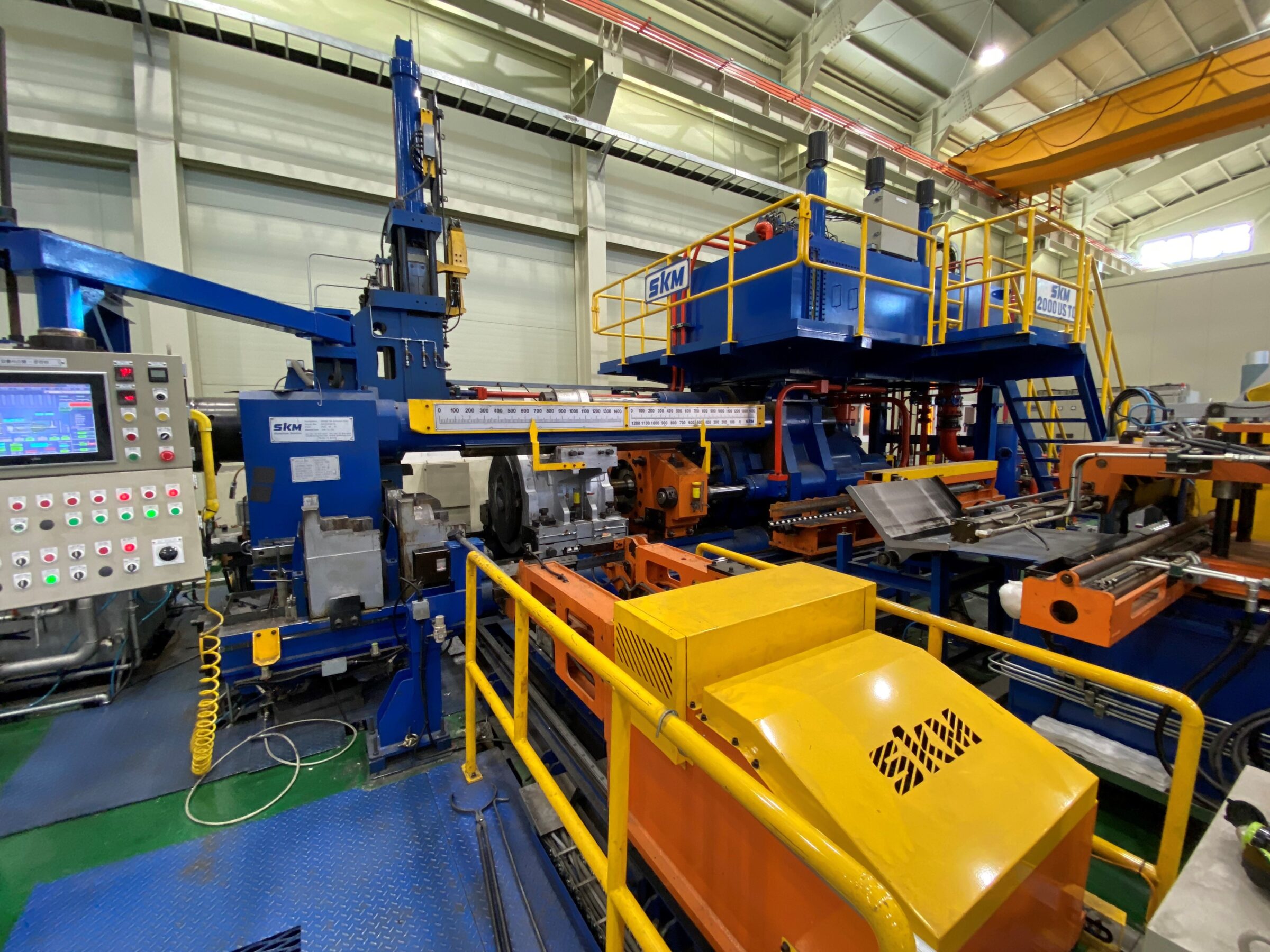 This image shows a large industrial environment with heavy machinery, including a blue and orange mechanical press and various metal components.