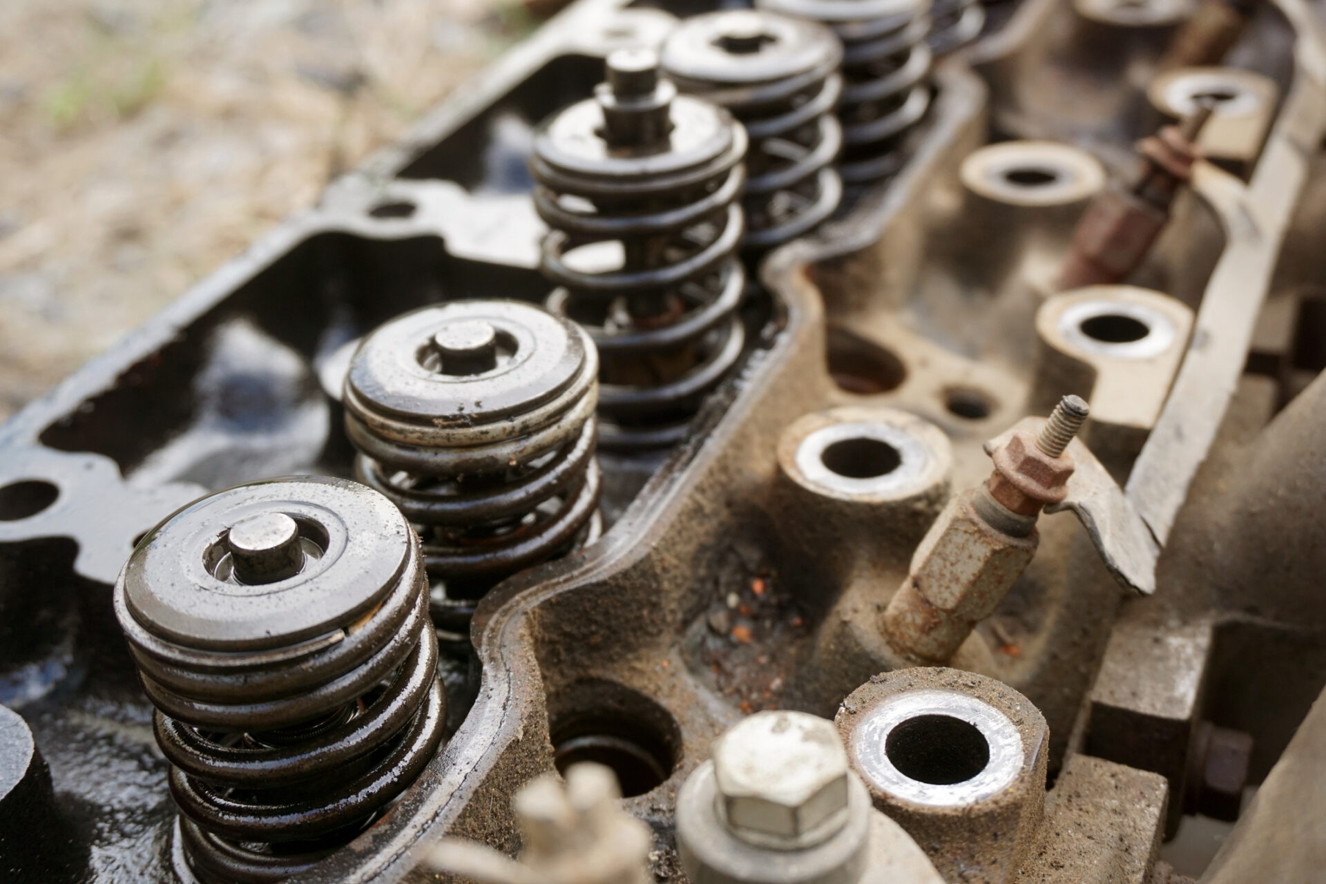 This image shows a close-up of a car engine's cylinder head, displaying valve springs and components, with signs of wear and rust.