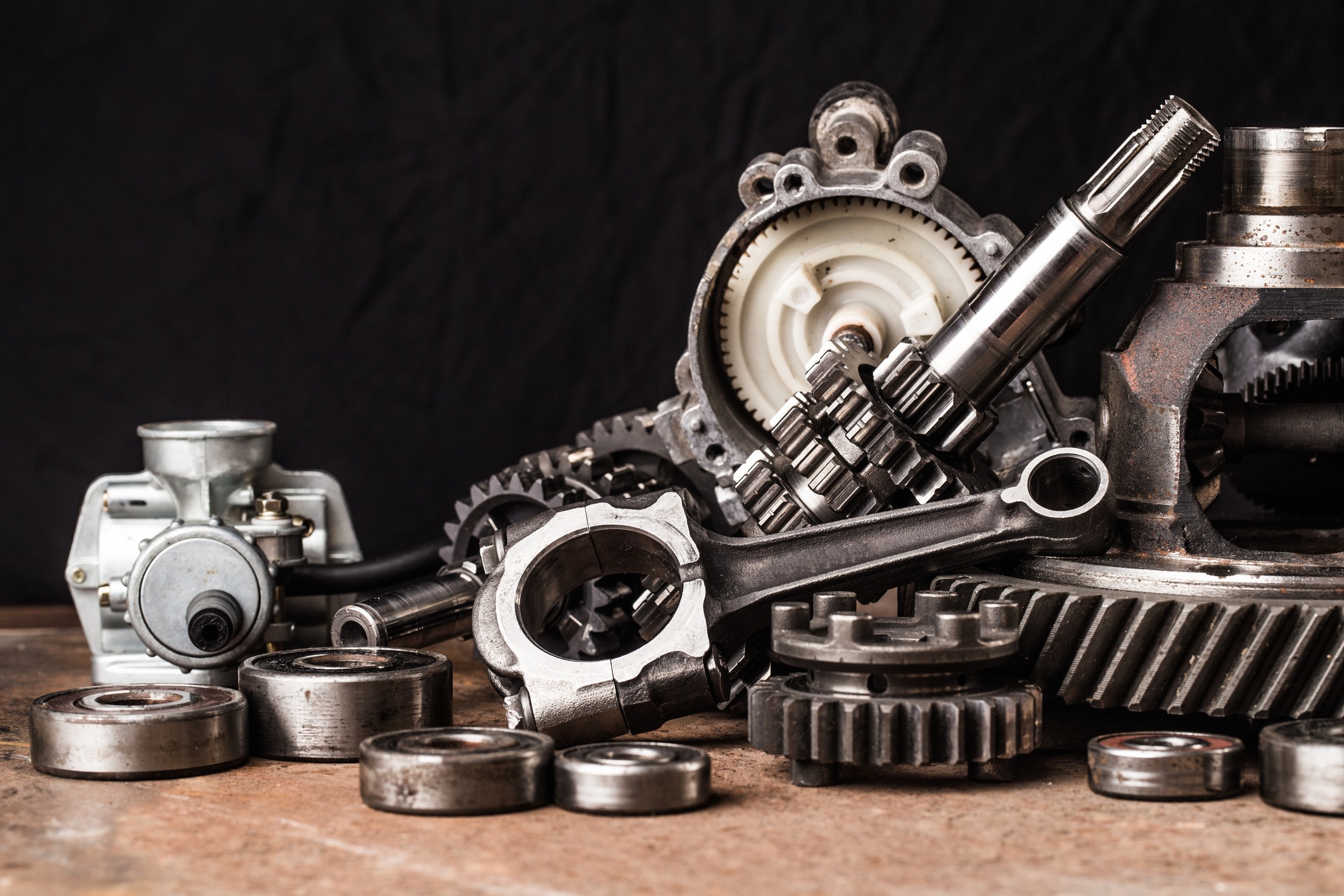 The image shows an assortment of metallic mechanical parts such as gears, bearings, and a carburetor, indicative of automotive or machinery equipment.