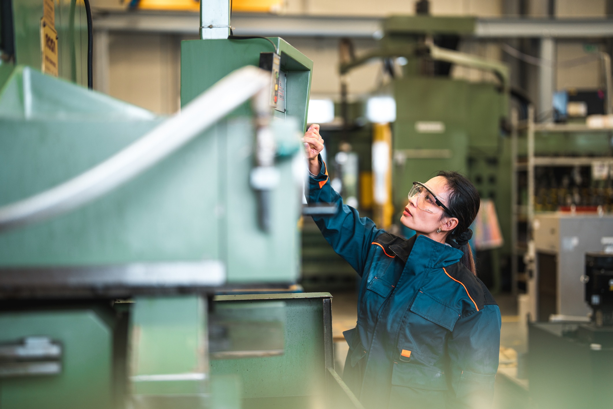 A person in safety glasses and workwear is operating machinery in an industrial setting, looking focused and attentive to the task.