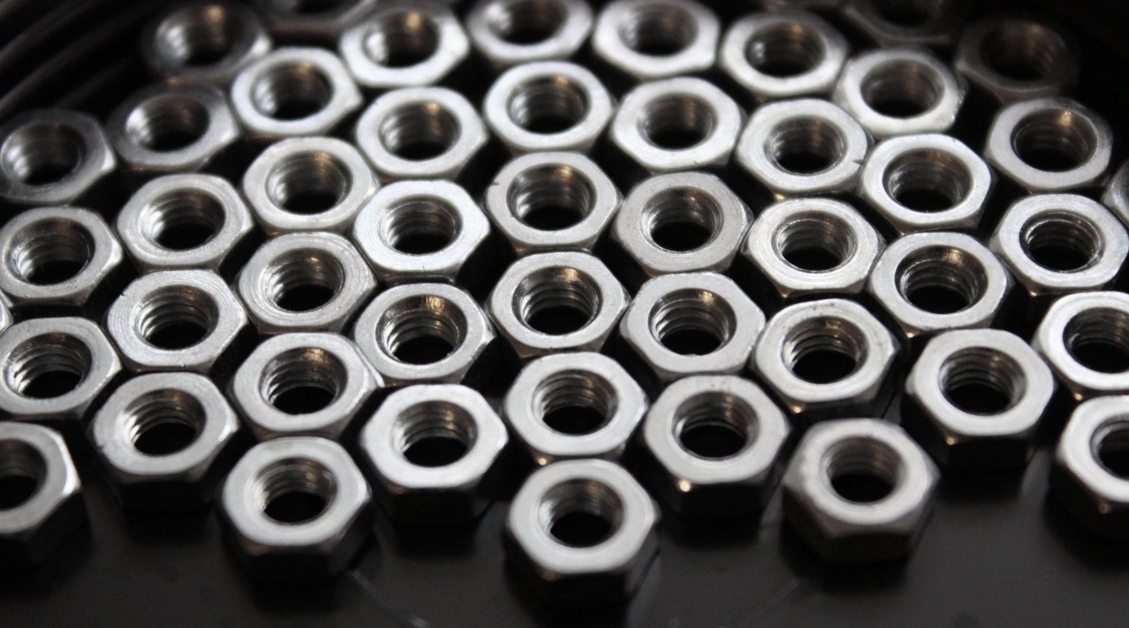 This image shows a collection of hexagonal metal nuts closely arranged in rows, with a clear focus on the threaded interior of each nut.