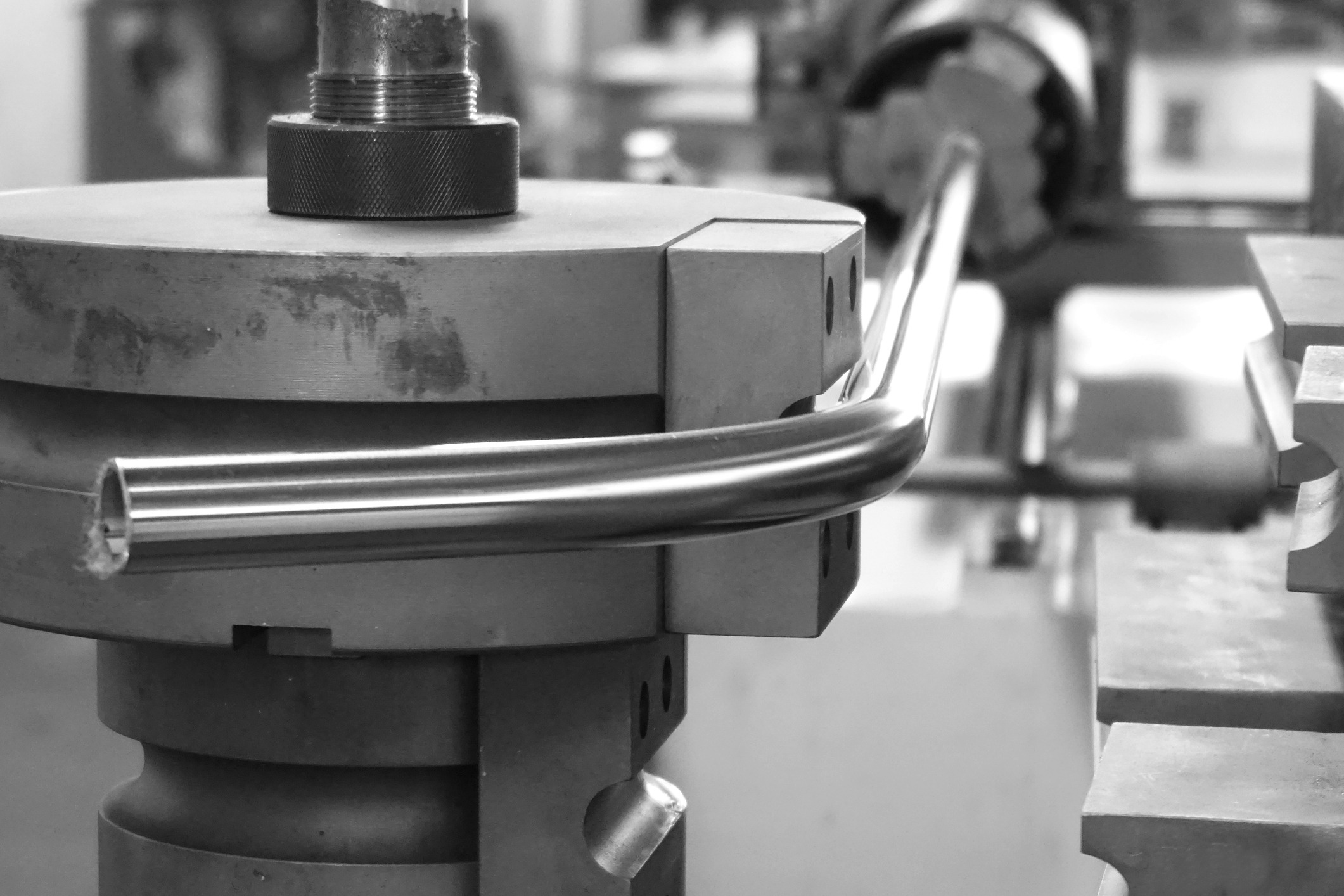 A black and white image shows industrial machinery bending a metal tube, reflecting precision engineering and manufacturing environment.